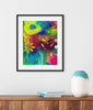 Framed colorful abstract art piece on a wall above a wooden shelf with a vase and books.