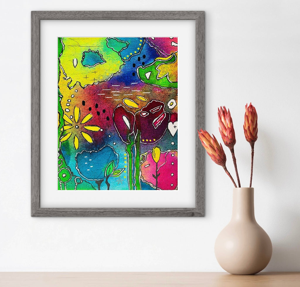 Framed colorful floral artwork on a white wall with a vase of dried flowers.