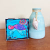 a turtle painting standing next to a blue vase with a seashell on it