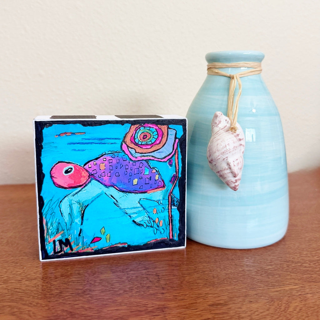 a turtle painting standing next to a blue vase with a seashell on it