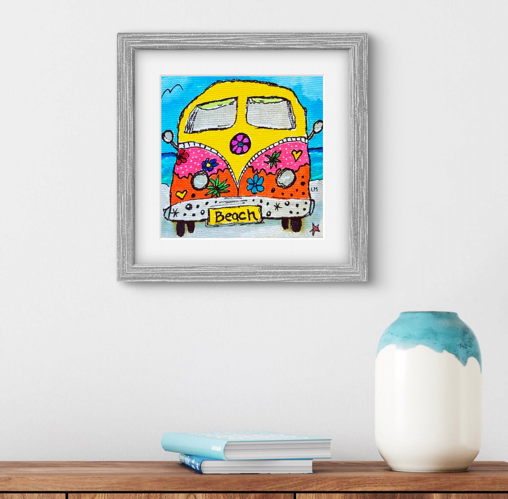 Framed artwork of a colorful van with 'Beach' text on a white wall with a vase and books below.